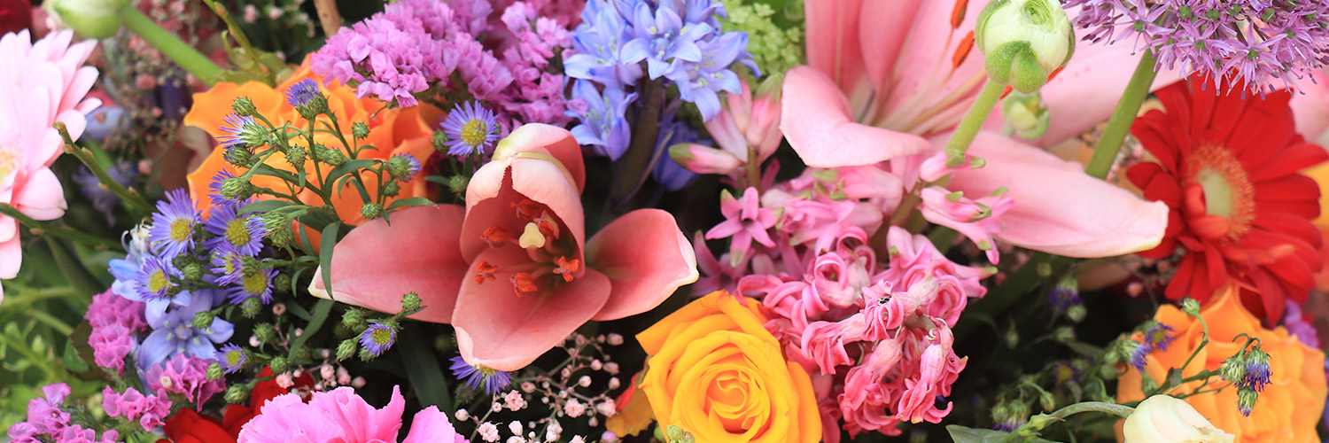 A vibrant bouquet of various flowers, including lilies, roses, and daisies, nestled against a backdrop of green leaves and small filler blooms.