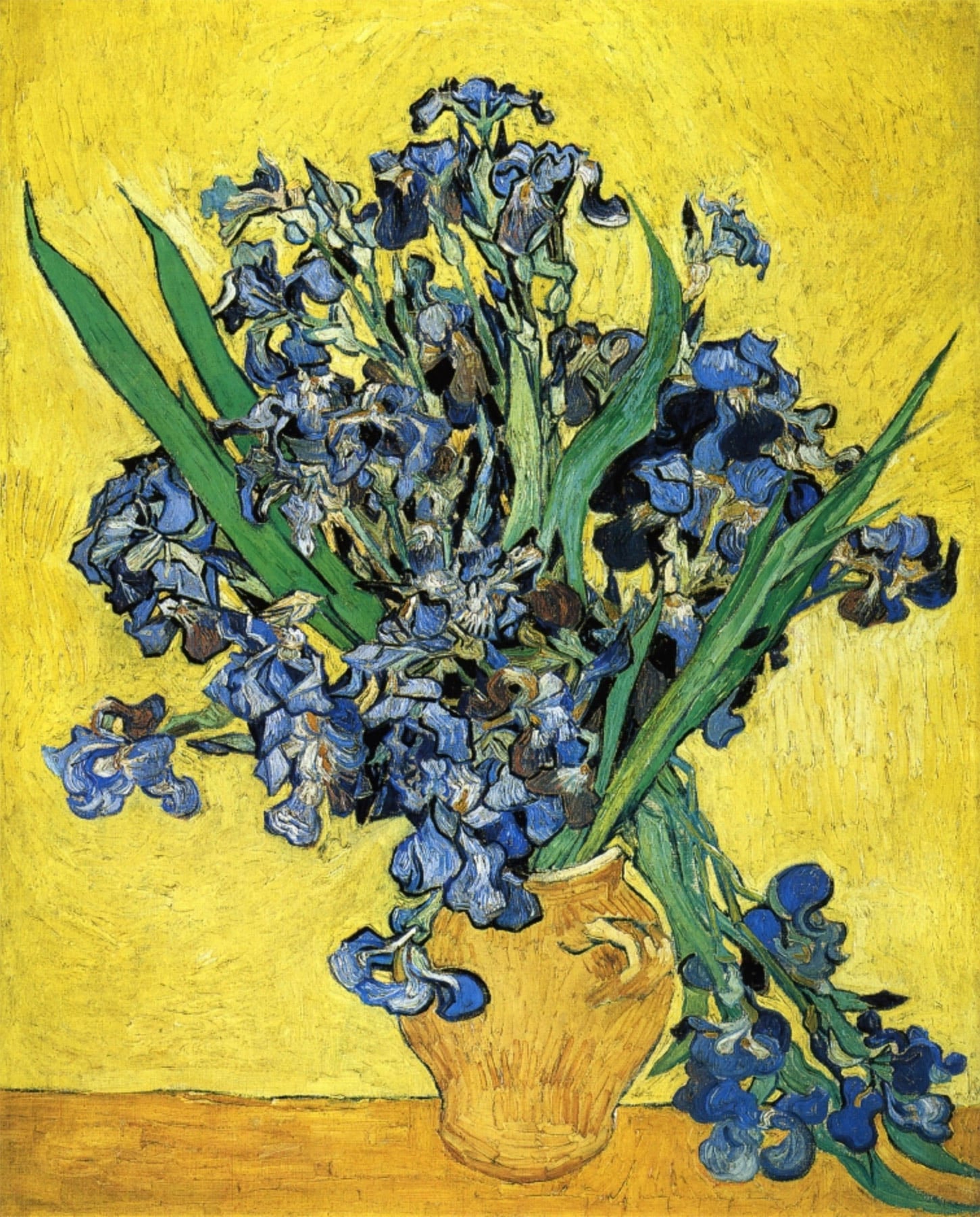 An image of Vincent Van Gog's oil painting, "Still Life with Irises." A yellow vase holds a bunch of vibrant blue irises with green leaves, set against a bright yellow background on a wooden table.