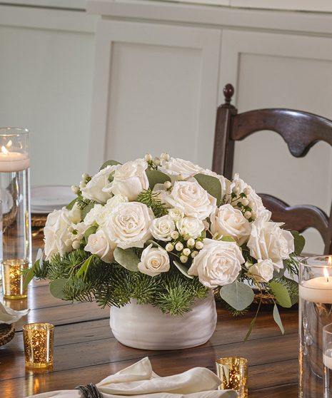 Winter White Rose Centerpiece featuring white mountain roses and hypericum berries nestled in winter  foliage.